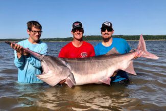 three men holding paddlefish