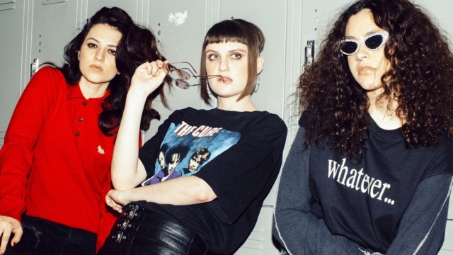 MUNA, three young women looking directly into the camera while leaning on school lockers.