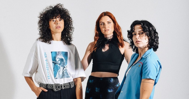 MUNA, three young women who are standing in a semi-circle and looking directly into the camera.